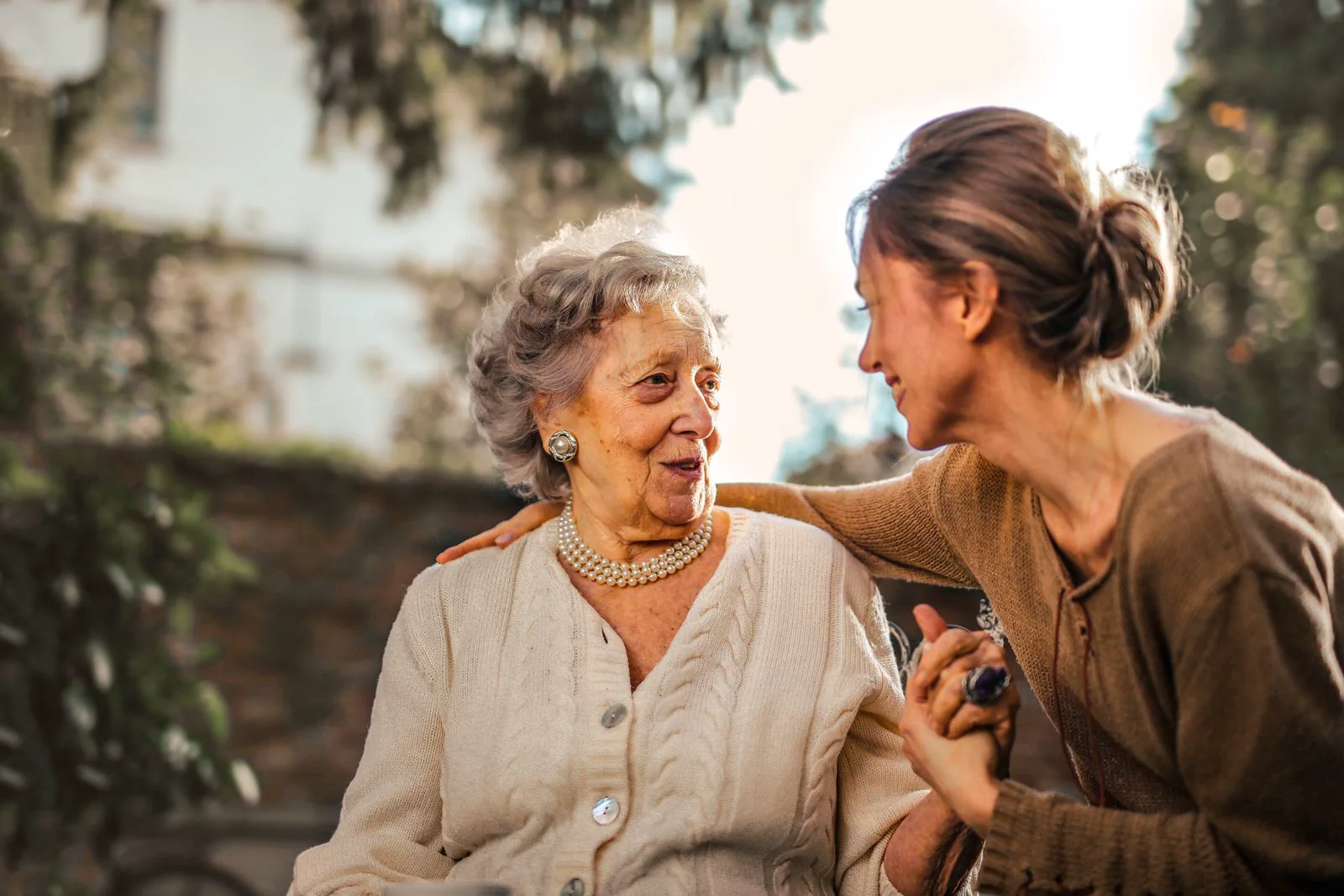 A caregiver sitting with an older woman, holding her hand in warm afternoon light.